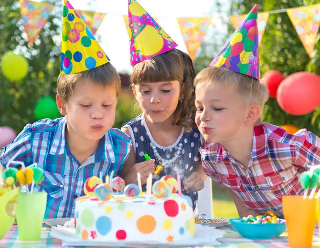 Three children blowing out candles on a birthday cake.